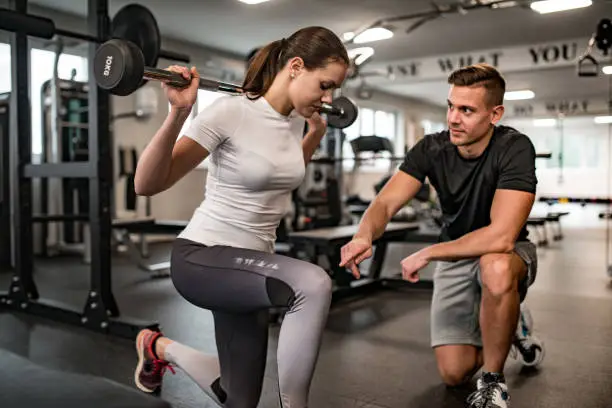 Fitness Instructor Guiding Young Woman When She Exercises. Rehabilitation vs. Personal Training: Striking the Balance for Athletes in NYC