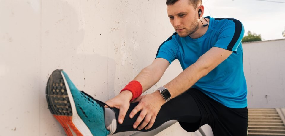 Caucasian man stretching city workout Young man runner getting ready to run stretching legs warm up quad stretch exercise on outdoor staircase
