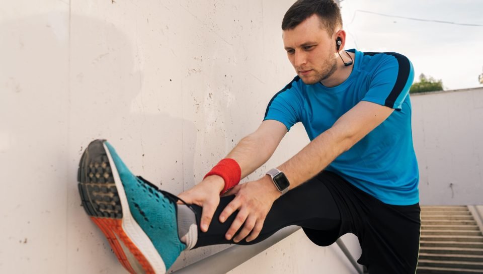 Young man runner getting ready to run stretching legs warm up quad stretch exercise on outdoor staircase