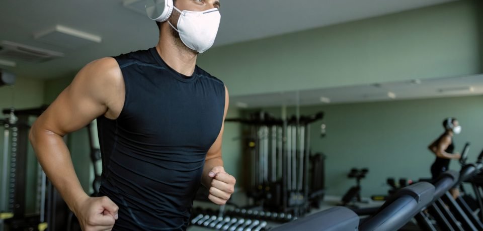 Athletic man with protective face mask jogging on running track Young sportsman wearing a face mask while running on treadmill at health club during coronavirus epidemic.